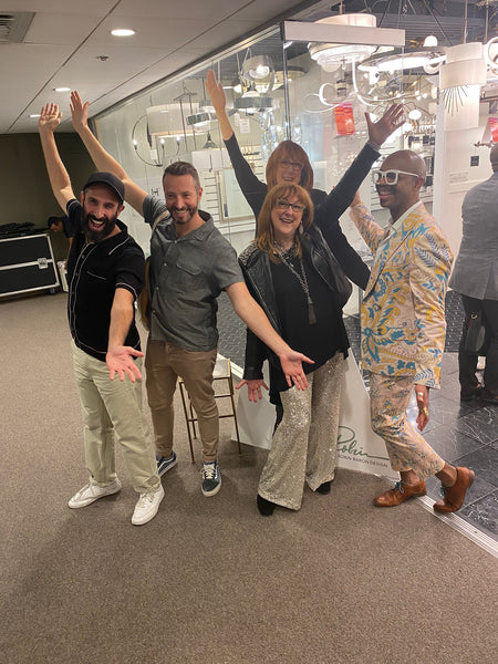 Robin Baron with guests at the lighting showroom, standing in a row with arms raised wide.