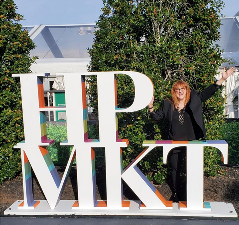 Robin poses behind a sculpture that reads: HPMKT