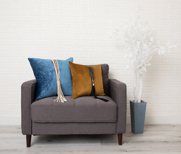 Picture of two pillows, one blue and one orange, with a zipper down their middle and a tassel, sitting on a loveseat.