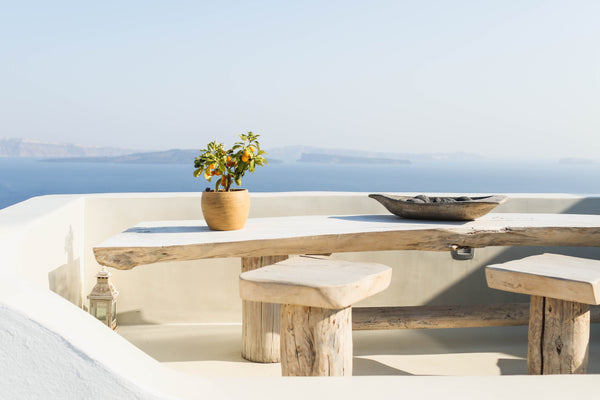 Image of a decorated outdoor space on a balcony next to water. A wooden table is decorated with a brown planter and a plant and a rustic decorative tray. Photo by Angela Pham on Unsplash