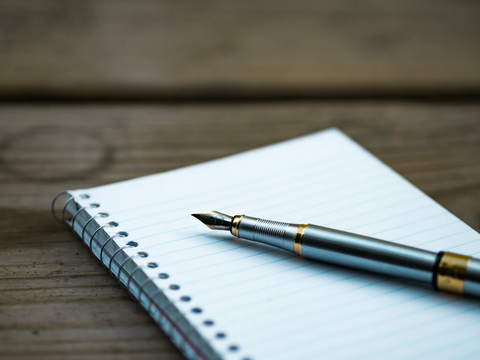 A fountain pen rests on a notebook on a wooden table